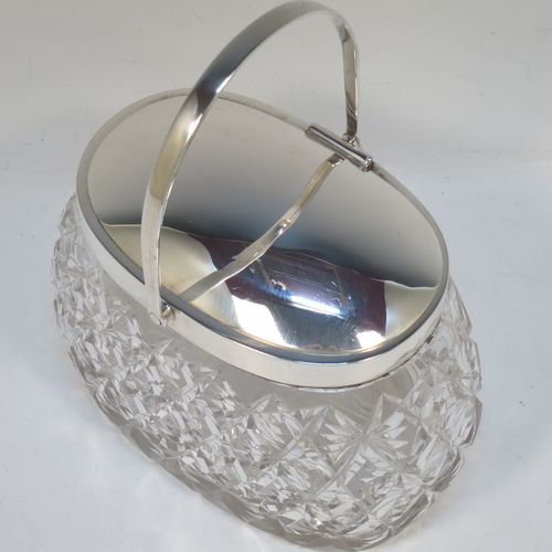 A very pretty and unusual Antique Victorian Sterling Silver and hand-cut crystal biscuit jar, having an oval crystal body with hand-cut hobnail and star-cut work, a plain oval mechanical lid which opens when moving the plain hinged swing-handle either left or right, and all sitting on a flat star-cut base. Made by Heath and Middleton of Birmingham in 1899. The dimensions of this fine hand-made antique silver and crystal biscuit jar are height (excluding handle) 13 cms (5 inches), length 16.5 cms (6.5 inches), and width 9 cms (3.5 inches).