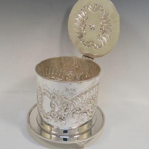 A very pretty Antique Victorian Silver-Plated biscuit box, having a round straight-sided body with bead-edged borders, hand-chased fluting, scroll, and floral decoration, a flat hinged lid with matching decoration and a cast round finial, and sitting on an attached base plate with three cast foliate feet. This beautiful antique silver-plated biscuit box was made by Harrison Brothers and Howson of Sheffield in ca. 1880. The dimensions of this fine hand-made antique silver-plated biscuit box are height 18 cms (7 inches), and diameter at base 19 cms (7.5 inches).