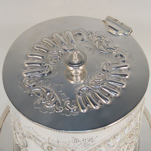 A very pretty Antique Victorian Silver-Plated biscuit box, having a round straight-sided body with bead-edged borders, hand-chased fluting, scroll, and floral decoration, a flat hinged lid with matching decoration and a cast round finial, and sitting on an attached base plate with three cast foliate feet. This beautiful antique silver-plated biscuit box was made by Harrison Brothers and Howson of Sheffield in ca. 1880. The dimensions of this fine hand-made antique silver-plated biscuit box are height 18 cms (7 inches), and diameter at base 19 cms (7.5 inches).