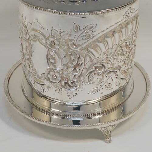 A very pretty Antique Victorian Silver-Plated biscuit box, having a round straight-sided body with bead-edged borders, hand-chased fluting, scroll, and floral decoration, a flat hinged lid with matching decoration and a cast round finial, and sitting on an attached base plate with three cast foliate feet. This beautiful antique silver-plated biscuit box was made by Harrison Brothers and Howson of Sheffield in ca. 1880. The dimensions of this fine hand-made antique silver-plated biscuit box are height 18 cms (7 inches), and diameter at base 19 cms (7.5 inches).