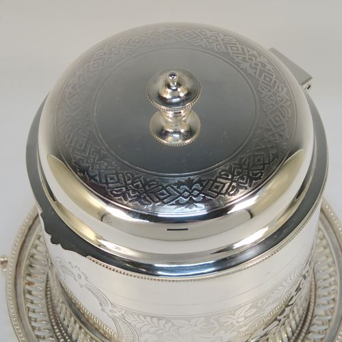 A very pretty Antique Victorian Silver-Plated biscuit box, having a round straight-sided body with bead-edged borders, hand-engraved floral decoration, a domed hinged lid with matching decoration and a cast round finial, and sitting on an attached base plate with three cast lions-paw  feet. This beautiful antique silver-plated biscuit box was made in ca. 1880. The dimensions of this fine hand-made antique silver-plated biscuit box are height 17 cms (6.75 inches), and diameter at base 18 cms (7 inches).   