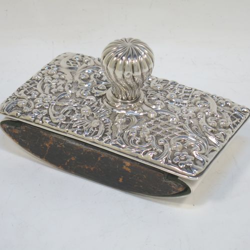 A very pretty Antique Edwardian Sterling Silver Rocker Blotter, having a rectangular body with rounded corners and hand-chased floral and scroll decoration, a leather covered rocker base, and a swirl fluted round handle that screws in to secure the rocker base and blotting paper to the upper body. Made by Henry Miller of Birmingham in 1902. The dimensions of this fine hand-made antique silver rocker blotter are length 11.5 cms (4.5 inches), height 6.5 cms (2.5 inches), and width 7 cms (2.75 inches).  