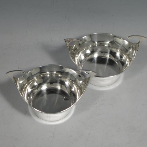 Antique Edwardian sterling silver pair of bon-bon dishes, having plain round bodies, with very unusual flying scroll handles, and each sitting on flat bases. Originally imported into, and hallmarked for, London in 1905. The dimensions of this fine pair of hand-made silver bon-bon dishes are width across handles 12 cms (4.75 inches), height 8 cms (3.25 inches), and they weigh a total of 180g (5.3 troy ounces).