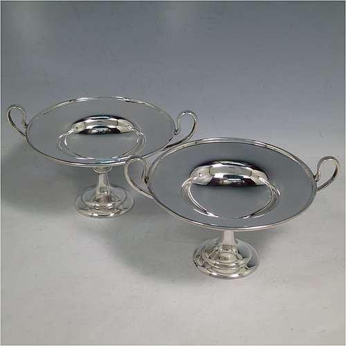 An Antique Edwardian Sterling Silver pair of bon-bon dishes, having plain round bodies, with applied reeded borders and two looped side handles, all raised above and sitting on plain round pedestal feet. Made by Holland, Aldwinkle & Slater  of London in 1907. The dimensions of these fine hand-made antique silver bon-bon dishes are height 9 cms (3.5 inches), diameter 11.5 cms (4.5 inches), and they weigh a total of approx. 241g (7.8 troy ounces).    