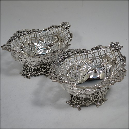 A very pretty Antique Victorian Sterling Silver pair of bon-bon baskets or dishes, having oval bodies with hand-pierced geometrical and scroll work decoration, an applied cast floral and scroll border, and sitting on matching pierced feet. Made by William Comyns of London in 1892. The dimensions of this fine hand-made pair of antique silver bon-bon dishes or baskets are length 16 cms (6.25 inches), width 12 cms (4.75 inches), height 7 cms (2.75 inches), and they weigh a total of  approx. 328g (10.6 troy ounces).    