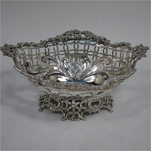 A very pretty Antique Victorian Sterling Silver pair of bon-bon baskets or dishes, having oval bodies with hand-pierced geometrical and scroll work decoration, an applied cast floral and scroll border, and sitting on matching pierced feet. Made by William Comyns of London in 1892. The dimensions of this fine hand-made pair of antique silver bon-bon dishes or baskets are length 16 cms (6.25 inches), width 12 cms (4.75 inches), height 7 cms (2.75 inches), and they weigh a total of approx. 328g (10.6 troy ounces).