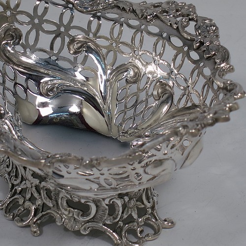 A very pretty Antique Victorian Sterling Silver pair of bon-bon baskets or dishes, having oval bodies with hand-pierced geometrical and scroll work decoration, an applied cast floral and scroll border, and sitting on matching pierced feet. Made by William Comyns of London in 1892. The dimensions of this fine hand-made pair of antique silver bon-bon dishes or baskets are length 16 cms (6.25 inches), width 12 cms (4.75 inches), height 7 cms (2.75 inches), and they weigh a total of approx. 328g (10.6 troy ounces).