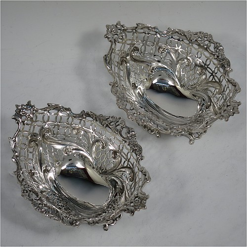 A very pretty Antique Victorian Sterling Silver pair of bon-bon baskets or dishes, having oval bodies with hand-pierced geometrical and scroll work decoration, an applied cast floral and scroll border, and sitting on matching pierced feet. Made by William Comyns of London in 1892. The dimensions of this fine hand-made pair of antique silver bon-bon dishes or baskets are length 16 cms (6.25 inches), width 12 cms (4.75 inches), height 7 cms (2.75 inches), and they weigh a total of approx. 328g (10.6 troy ounces).