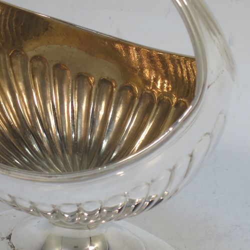 A small but very unusual and pretty Antique Georgian Sterling Silver bon-bon dish or sweet-meat basket, having an oval body with hand-chased half-fluted decoration, a gold-gilt interior, an overhead loop handle, and all sitting on a pedestal foot. Made in London in 1802. The dimensions of this fine hand-made antique bon-bon dish or basket are length 8 cms (3 inches), height 10 cms (4 inches), width 7 cms (2.75 inches), and it weighs approx. 104g (3.4 troy ounces)