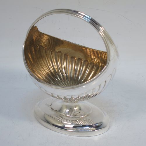 A small but very unusual and pretty Antique Georgian Sterling Silver bon-bon dish or sweet-meat basket, having an oval body with hand-chased half-fluted decoration, a gold-gilt interior, an overhead loop handle, and all sitting on a pedestal foot. Made in London in 1802. The dimensions of this fine hand-made antique bon-bon dish or basket are length 8 cms (3 inches), height 10 cms (4 inches), width 7 cms (2.75 inches), and it weighs approx. 104g (3.4 troy ounces)