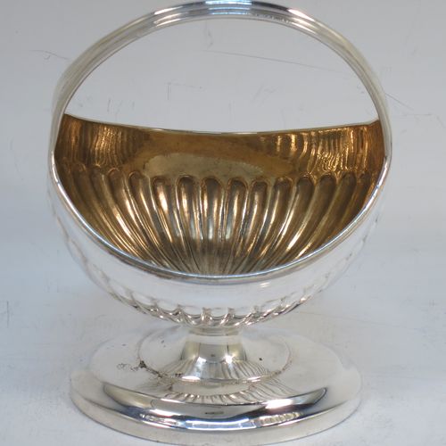 A small but very unusual and pretty Antique Georgian Sterling Silver bon-bon dish or sweet-meat basket, having an oval body with hand-chased half-fluted decoration, a gold-gilt interior, an overhead loop handle, and all sitting on a pedestal foot. Made in London in 1802. The dimensions of this fine hand-made antique bon-bon dish or basket are length 8 cms (3 inches), height 10 cms (4 inches), width 7 cms (2.75 inches), and it weighs approx. 104g (3.4 troy ounces)