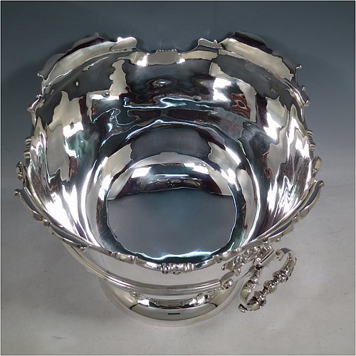 An Antique Edwardian Sterling Silver large table bowl, having a round body with an applied shell and scroll border, an applied reeded central band, together with cast hinged side-handles, and with applied strap-work on the lower body, and all sitting on a pedestal foot. Made by Williams of Birmingham in 1909. The dimensions of this fine hand-made large silver table bowl are diameter 29 cms (11.5 inches), height 23.5 cms (9.25 inches), and it weighs approx. 2,123g (68.5 troy ounces).