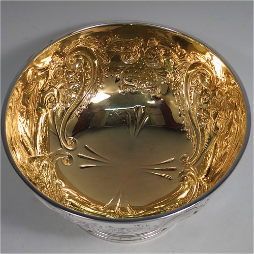 A very pretty Antique Edwardian Sterling Silver large table bowl, having a round body with an applied reeded border and hand-chased floral and scroll decoration, with two vacant cartouches either side, a gold-gilt interior, and all sitting on a stepped pedestal foot. Made by the Deakin Brothers of Sheffield in 1904. The dimensions of this fine hand-made antique silver bowl are diameter 25.5 cms (10 inches), height 15 cms (6 inches), and it weighs approx. 780g (25 troy ounces).