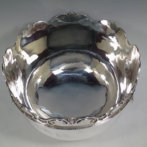 A very handsome and large Antique Edwardian Sterling Silver Montieth style bowl, having a plain round body with an applied scroll border, together with two cast lion-mask side-handles, and sitting on a pedestal foot. Made by William Comyns of London in 1902. The dimensions of this fine hand-made antique silver Montieth table bowl are diameter 31 cms (12 inches), height 23 cms (9 inches), and it weighs approx. 2,440g (78.7 troy ounces).