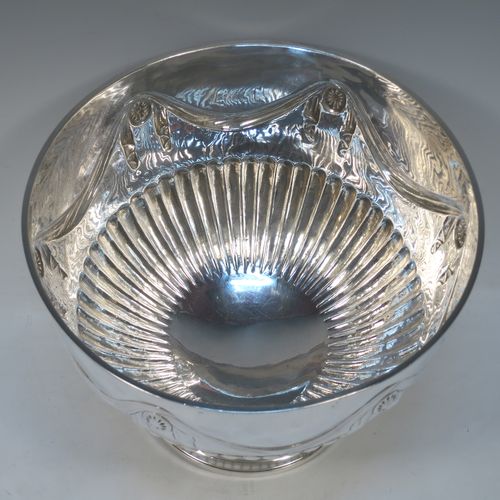 A very pretty Antique Victorian Sterling Silver large Rose bowl, having a round body with hand-chased half fluted decoration, an applied reeded rim above another band of hand-chased swags and bows, and sitting on a pedestal foot with matching fluting. Made by Gibson and Langman of London in 1890. The dimensions of this fine hand-made antique silver large table bowl are diameter 24 cms (9.5 inches), height 20 cms (8 inches), and it weighs approx. 965g (31 troy ounces).