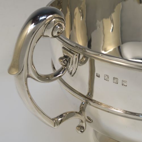 A large and very handsome Antique Edwardian Scottish Sterling Silver two-handled table bowl, having a plain round bellied body, with two cast flying scroll side-handles, an applied top border and central girdle, and all sitting on a plain round pedestal foot. This elegant traditional two-handled silver bowl or trophy was made by Lawson and Co., of Glasgow in 1902. The dimensions of this fine hand-made antique silver bowl are width across handles 37 cms (14.5 inches), diameter of main body 25.5 cms (10 inches), height 19 cms (7.5 inches), and it weighs approx. 1,532g (49.5 troy ounces).