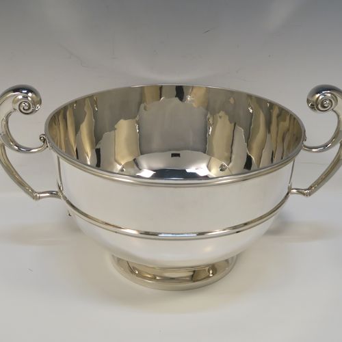 A large and very handsome Antique Edwardian Scottish Sterling Silver two-handled table bowl, having a plain round bellied body, with two cast flying scroll side-handles, an applied top border and central girdle, and all sitting on a plain round pedestal foot. This elegant traditional two-handled silver bowl or trophy was made by Lawson and Co., of Glasgow in 1902. The dimensions of this fine hand-made antique silver bowl are width across handles 37 cms (14.5 inches), diameter of main body 25.5 cms (10 inches), height 19 cms (7.5 inches), and it weighs approx. 1,532g (49.5 troy ounces).