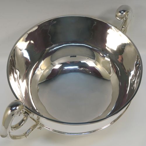 A large and very handsome Antique Edwardian Scottish Sterling Silver two-handled table bowl, having a plain round bellied body, with two cast flying scroll side-handles, an applied top border and central girdle, and all sitting on a plain round pedestal foot. This elegant traditional two-handled silver bowl or trophy was made by Lawson and Co., of Glasgow in 1902. The dimensions of this fine hand-made antique silver bowl are width across handles 37 cms (14.5 inches), diameter of main body 25.5 cms (10 inches), height 19 cms (7.5 inches), and it weighs approx. 1,532g (49.5 troy ounces).