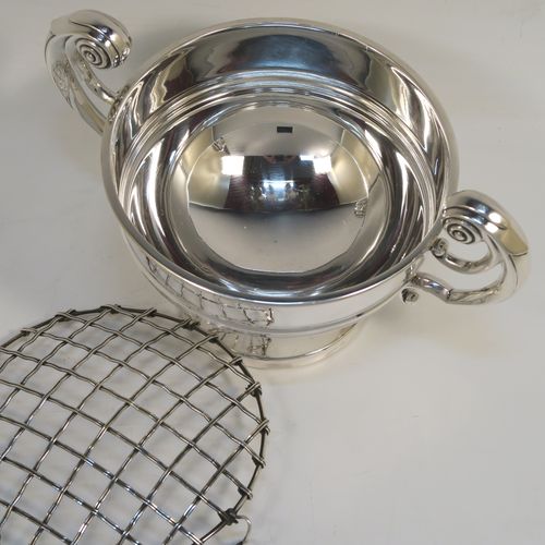 A handsome classical style Sterling Silver Rose bowl, having a round plain body with an applied reeded border, and a central applied band, with two flying scroll side handles, and sitting on a round pedestal foot, together with its original metal rose grill. This elegant silver rose bowl was made by Walker and Hall of Sheffield in 1934. The dimensions of this fine hand-made silver two-handled bowl are height (inc. handles) 11 cms (4.3 inches), diameter 12.5 cms (5 inches), and it weighs approx. 300g (9.7 troy ounces).