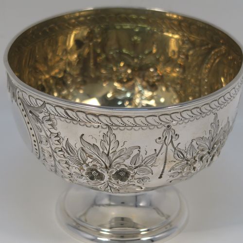 A very pretty Antique Victorian Sterling Silver rose bowl, having a round body with hand-chased swags of floral decoration surrounding two vacant round cartouches on either side, with an applied reed-edged border, a gold-gilt interior, and all sitting on a plain round pedestal foot. This beautiful silver bowl was made by Walker and Hall of Sheffield in 1885. The dimensions of this fine hand-made antique silver bowl are diameter 11 cms (4.25 inches), height 8 cms (3 inches), and it weighs approx. 134g (4.3 troy ounces).