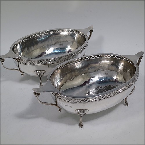 A very unusual and pretty pair of Arts and Crafts style Sterling Silver bowls, having oval bodies with hand-hammered decoration, with hand-pierced and floral borders, two scroll side-handles with flat thumb-pieces, and all sitting on four cast goat hoof feet. Made by A. E. Jones of Birmingham in 1921. The dimensions of these fine hand-made Arts and Crafts silver oval bowls are length 21 cms (8.25 inches), width 11 cms (4.3 inches), height 6.5 cms (2.5 inches), and they weigh a total of approx. 470g (15.2 troy ounces).    