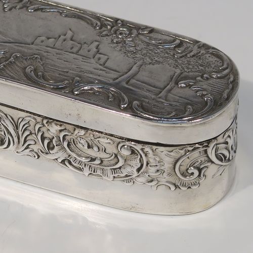 A very pretty Antique Edwardian Sterling Silver table box, having a long rectangular body with rounded ends, with a hinged lid having a hand-chased figural and pastoral scene, a band of floral and scroll decoration on the sides, a gold-gilt interior, and sitting on a flat base. This beautiful silver dressing table box bears a sterling importers mark for John George Piddington of London in 1907. The dimensions of this fine hand-made antique silver table box are length 17 cms (6.75 inches), width 3.5 cms (1.3 inches), height 3 cms (1 inch), and it weighs approx. 151g (4.9 troy ounces).
