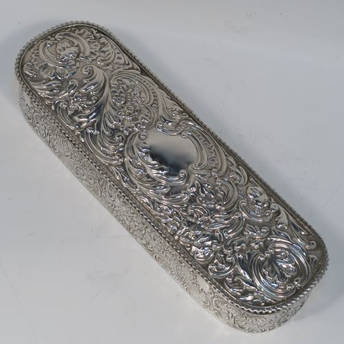 A bold and very pretty Antique Edwardian Sterling Silver table box, having a rounded rectangular body with hand-chased floral and scroll decoration, a hinged lid with matching decoration surrounding a vacant central cartouche, an applied rope-twist top border, a gold-gilt interior with three compartments, and sitting on a flat base. This beautiful silver dressing table box was made by Charles Boyton of Birmingham in 1904. The dimensions of this fine hand-made antique silver table box are length 22 cms (8.75 inches), width 6.5 cms (2.5 inches), height 4 cms (1.5 inches), and it weighs approx. 269g (8.7 troy ounces).