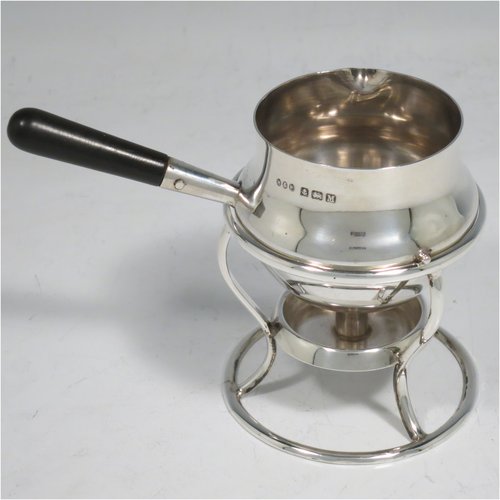 A Sterling Silver brandy saucepan warmer on burner stand, having a plain round baluster body, a sparrow-beak spout, an original wood turned handle, and sitting on a wire-work frame with integral spirit burner. Made by Hukin & Heath of Birmingham in 1936. The dimensions of this fine hand-made silver brandy warmer are height 8 cms (3.25 inches), length (inc. handle) 12 cms (4.75 inches), and it weighs approx. 105g (3.4 troy ounces).   