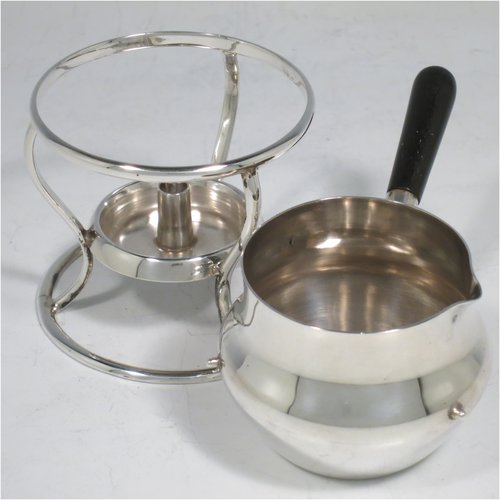 A Sterling Silver brandy saucepan warmer on burner stand, having a plain round baluster body, a sparrow-beak spout, an original wood turned handle, and sitting on a wire-work frame with integral spirit burner. Made by Hukin & Heath of Birmingham in 1936. The dimensions of this fine hand-made silver brandy warmer are height 8 cms (3.25 inches), length (inc. handle) 12 cms (4.75 inches), and it weighs approx. 105g (3.4 troy ounces).