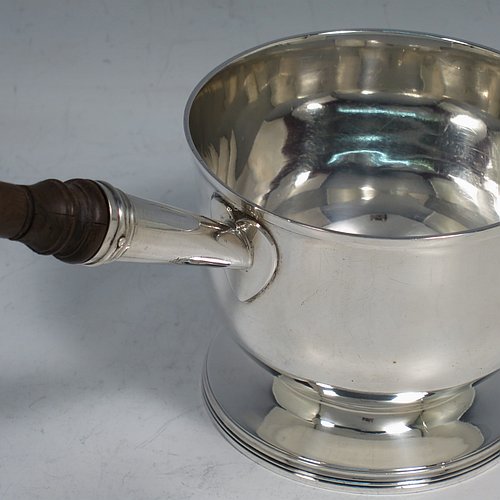An Antique Georgian Sterling Silver brandy saucepan warmer, having a plain round body with tucked-under belly, an original pinned wood turned handle with heart-shaped cut-card mount, and all sitting on a reeded pedestal foot. Made by John Emes of London in 1805. The dimensions of this fine hand-made brandy saucepan warmer are height of main body 7.5 cms (3 inches), length (inc. handle) 22 cms (8.75 inches), and it weighs approx. 202g (6.5 troy ounces).