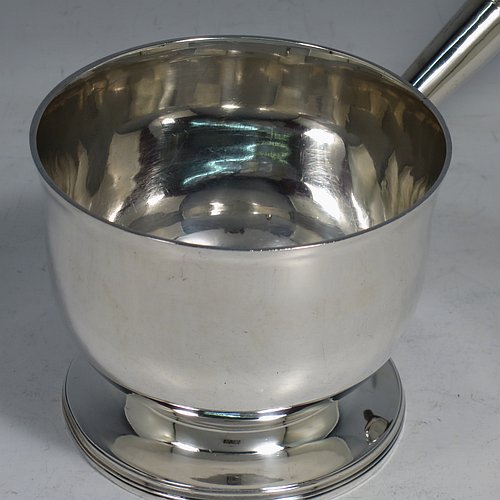 An Antique Georgian Sterling Silver brandy saucepan warmer, having a plain round body with tucked-under belly, an original pinned wood turned handle with heart-shaped cut-card mount, and all sitting on a reeded pedestal foot. Made by John Emes of London in 1805. The dimensions of this fine hand-made brandy saucepan warmer are height of main body 7.5 cms (3 inches), length (inc. handle) 22 cms (8.75 inches), and it weighs approx. 202g (6.5 troy ounces).