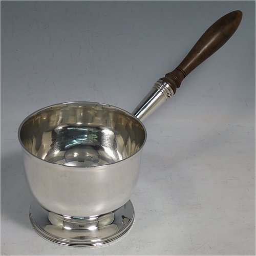 An Antique Georgian Sterling Silver brandy saucepan warmer, having a plain round body with tucked-under belly, an original pinned wood turned handle with heart-shaped cut-card mount, and all sitting on a reeded pedestal foot. Made by John Emes of London in 1805. The dimensions of this fine hand-made brandy saucepan warmer are height of main body 7.5 cms (3 inches), length (inc. handle) 22 cms (8.75 inches), and it weighs approx. 202g (6.5 troy ounces).