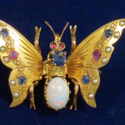 An Antique Victorian Aesthetic 9ct carat gold brooch, in the shape of a butterfly, with unusual mechanical articulated clasp on reverse, and having small rubies, sapphires, and pearls on the wings, with the eyes as rubies, the thorax as a larger sapphire, and the abdomen as an oval opal. Made in ca. 1880. The dimensions of this fine antique gold butterfly brooch are length 2 cms (0.75 inches), width 3 cms (1.25 inch), and it weighs approx. 3g.