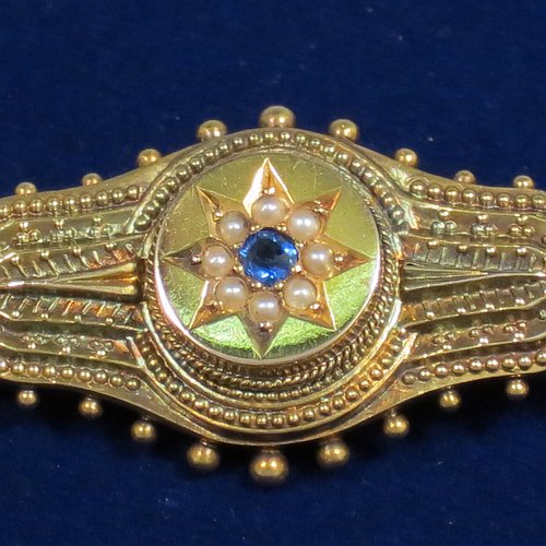 An Antique Victorian Etruscan style 15ct carat gold brooch, having an elongated and shaped oval body, with applied bead decoration, and a stepped round centre with star decoration having a sapphire and small pearls, and the back having a pin and a security ring but no chain. Made in ca. 1880. The dimensions of this fine antique gold brooch are length 4.5 cms (1.75 inches), width 2 cms (0.75 inch), and it weighs approx. 3.5g.