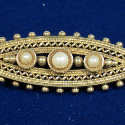 An Antique Victorian Etruscan style 15ct carat gold brooch, having an elongated oval body, with applied bead decoration, and a centre with three old graduated pearls, and the back having a security pin. Made in ca. 1880. The dimensions of this fine antique gold brooch are length 5 cms (2 inches), width 2 cms (0.75 inch), and it weighs approx. 4.8g.