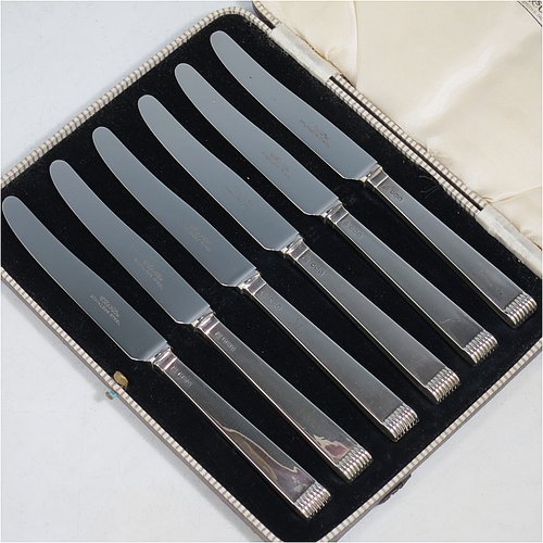 A Sterling Silver Art Deco style set of six butter or tea knives, having plain rectangular cross-section handles with reeded terminals, and plain finger-point stainless steel blades, all in their original cream satin and black velvet-lined presentation box. Made by Charles Boyton & Sons of Sheffield in 1939. The dimensions of this fine hand-made set of tea or butter knives are length of each knife 18 cms (7 inches), and the total weight is approx. 120g (4 troy ounces).