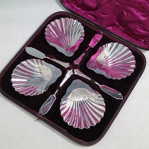 An Antique Victorian Sterling Silver set of four butter shells, having traditional scallop shapes, and sitting on three cast shell feet, together with four original butter knives in the Albany pattern, and all sitting in an original purple satin and velvet-lined presentation box. All made by Frances Higgins of London in 1884. The dimensions of this fine hand-made set of antique silver butter shells are length 12 cms (4.75 inches), width 10 cms (4 inches), with a total weight of approx. 385g (12.4 troy ounces).