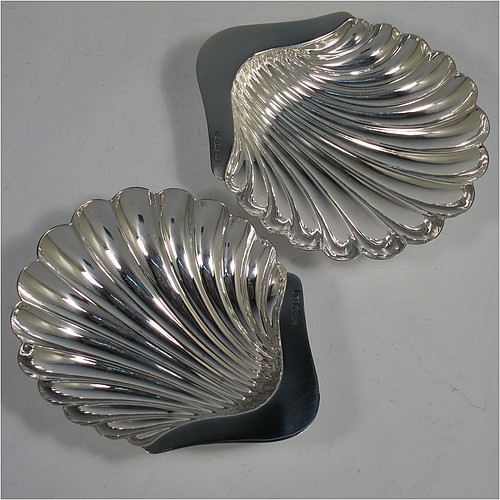An Antique Sterling Silver pair of butter shells, having hand-chased scalloped bodies, plain shaped thumb-pieces, and both sitting on three ball feet. All made by Henry Atkins of Sheffield in 1913. The dimensions of these fine hand-made antique silver butter dishes are length 12 cms (4.75 inches), width 10 cms (4 inches), height 2.5 cms (1 inch), and they have a total weight of approx. 113g (3.6 troy ounces).