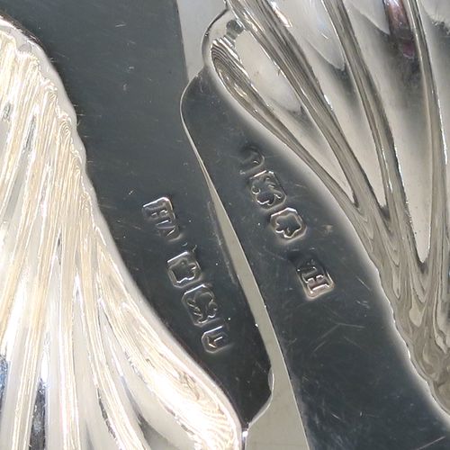 A handsome Antique Edwardian Sterling Silver pair of butter shells, having hand-chased scalloped bodies, plain shaped thumb-pieces, and both sitting on three ball feet. These beautiful silver shell butter dishes were made by Henry Atkins of Sheffield in 1909. The dimensions of these fine hand-made antique silver butter dishes are length 12 cms (4.75 inches), width 10 cms (4 inches), and they have a total weight of approx. 115g (3.7 troy ounces).