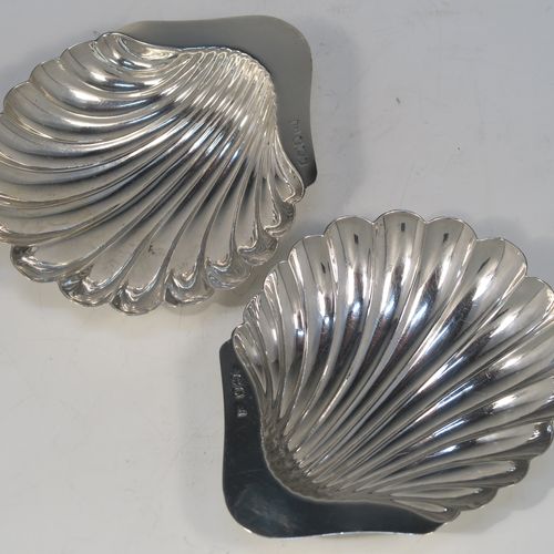 A handsome Antique Edwardian Sterling Silver pair of butter shells, having hand-chased scalloped bodies, plain shaped thumb-pieces, and both sitting on three ball feet. These beautiful silver shell butter dishes were made by Henry Atkins of Sheffield in 1909. The dimensions of these fine hand-made antique silver butter dishes are length 12 cms (4.75 inches), width 10 cms (4 inches), and they have a total weight of approx. 115g (3.7 troy ounces).
