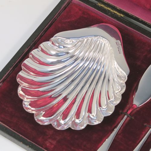 An elegant Antique Victorian Sterling Silver pair of butter shells, having traditional scallop shapes, and sitting on three cast ball feet, together with a pair of original butter knives in the Old English pattern, and all sitting in an original maroon satin and velvet-lined presentation box. This handsome pair of silver butter shells and knives were all made by the Atkin Brothers of Sheffield in 1900. The dimensions of this fine hand-made set of antique silver butter shells and knives are length 12 cms (4.75 inches), width 10 cms (4 inches), with a total weight of approx. 136g (4.4 troy ounces).