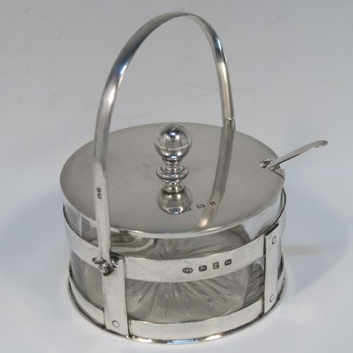 A very unusual Antique Victorian Sterling Silver and crystal butter, jam or honey dish and cover in an Arts and Crafts style, having a plain round galleried body with a hand-cut crystal liner and a swing-handle, a lift-off plain round cover with ball finial, and all sitting in a flat base, together with a matching condiment spoon . This elegant antique silver jam, honey or butter dish and cover was made by Norton and White of Birmingham in 1900. The matching spoon was made in Birmingham in 1906. The dimensions of this fine hand-made antique Arts and Crafts style silver covered dish are diameter 9 cms (3.5 inches), height (inc. handles) 12 cms (4.75 inches), with a total weight of approx. 200g (6.5 troy ounces).   