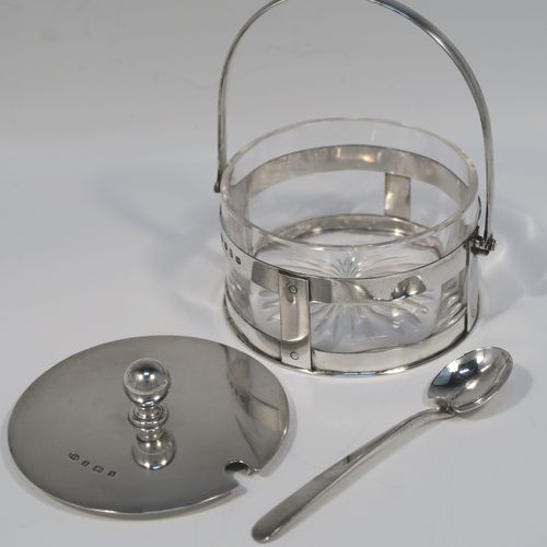 A very unusual Antique Victorian Sterling Silver and crystal butter, jam or honey dish and cover in an Arts and Crafts style, having a plain round galleried body with a hand-cut crystal liner and a swing-handle, a lift-off plain round cover with ball finial, and all sitting in a flat base, together with a matching condiment spoon . This elegant antique silver jam, honey or butter dish and cover was made by Norton and White of Birmingham in 1900. The matching spoon was made in Birmingham in 1906. The dimensions of this fine hand-made antique Arts and Crafts style silver covered dish are diameter 9 cms (3.5 inches), height (inc. handles) 12 cms (4.75 inches), with a total weight of approx. 200g (6.5 troy ounces).