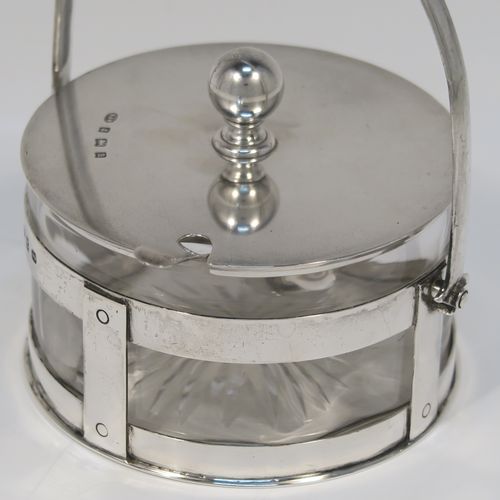 A very unusual Antique Victorian Sterling Silver and crystal butter, jam or honey dish and cover in an Arts and Crafts style, having a plain round galleried body with a hand-cut crystal liner and a swing-handle, a lift-off plain round cover with ball finial, and all sitting in a flat base, together with a matching condiment spoon . This elegant antique silver jam, honey or butter dish and cover was made by Norton and White of Birmingham in 1900. The matching spoon was made in Birmingham in 1906. The dimensions of this fine hand-made antique Arts and Crafts style silver covered dish are diameter 9 cms (3.5 inches), height (inc. handles) 12 cms (4.75 inches), with a total weight of approx. 200g (6.5 troy ounces).