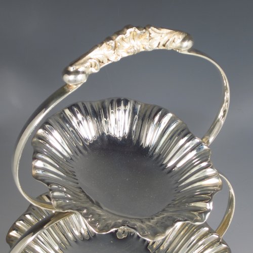 An Antique Victorian Art Nouveau style silver plated three-tier cake stand, having a graduated suite of three removable plates with hand-chased and fluted oval bodies, sitting within a very pretty tapering looped frame with cast shell-work handle and scroll feet. Made by Walker & Hall of Sheffield in ca. 1890. The dimensions of this fine hand-made silver-plated cake stand are height 42 cms (16.3 inches), width of frame at its widest point 25.5 cms (10 inches), and length of largest plate at base 25.5 cms (10 inches).