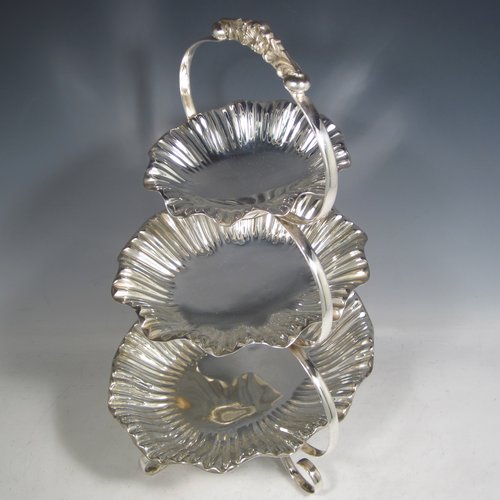 An Antique Victorian Art Nouveau style silver plated three-tier cake stand, having a graduated suite of three removable plates with hand-chased and fluted oval bodies, sitting within a very pretty tapering looped frame with cast shell-work handle and scroll feet. Made by Walker & Hall of Sheffield in ca. 1890. The dimensions of this fine hand-made silver-plated cake stand are height 42 cms (16.3 inches), width of frame at its widest point 25.5 cms (10 inches), and length of largest plate at base 25.5 cms (10 inches).