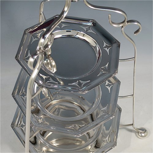 An Antique Edwardian pretty silver-plated cake stand, having three removable and graduated octagonal dishes with hand-pierced borders, all held in a wire-work frame with an oval carrying handle over scroll-work, and sitting on three bun feet. All made in ca. 1900. The dimensions of this fine hand-made antique silver-plated cake stand are height 45 cms (17.75 inches), width 30 cms (11.75 inchs), and the diameter of the dishes vary from 16.5 cms (6.5 inches) to 22 cms (8.6 inches).
