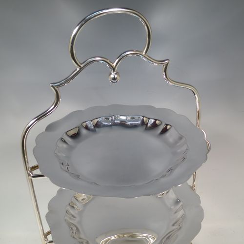 A pretty Antique Edwardian silver plated three-tier cake stand, having a suite of three plain removable plates with wavey-edged borders, sitting within a very pretty wire-work frame with scroll-work handle and four cast bun feet. Made in Sheffield in ca. 1910. The dimensions of this fine hand-made antique silver-plated cake stand are height 43 cms (17 inches), width at base 23 cms (9 inches), and diameter of plates 20 cms (8 inches).