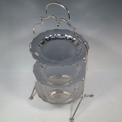 A pretty Antique Edwardian silver plated three-tier cake stand, having a suite of three plain removable plates with wavey-edged borders, sitting within a very pretty wire-work frame with scroll-work handle and four cast bun feet. Made in Sheffield in ca. 1910. The dimensions of this fine hand-made antique silver-plated cake stand are height 43 cms (17 inches), width at base 23 cms (9 inches), and diameter of plates 20 cms (8 inches).
