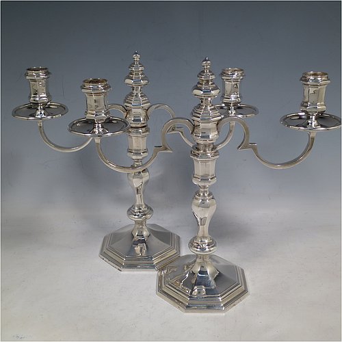 A Sterling Silver cast pair of George II style two-light candelabra, having octagonal panelled and baluster style bodies with reeded borders, removable scroll arms with nozzles and drip pans, and a central finial. Made in Birmingham in 1974. The dimensions of this fine hand-made pair of silver candelabra are height 24 cms (9.5 inches), spread across arms 25.5 cms (10 inches), and with a total weight of approx. 1,418g (45.7 troy ounces). Please note that these candelabra are all cast and not filled.   